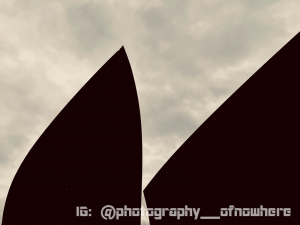 black and white photo of sail-shaped silhouettes against cloudy sky
