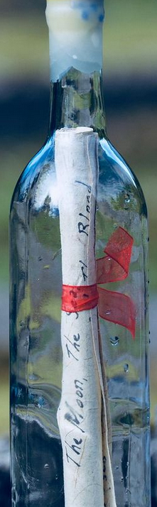 piece of paper with writing on it, tied with a ribbon inside glass bottle
