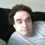 Person with pale skin and short dark hair, wearing gray T-shirt